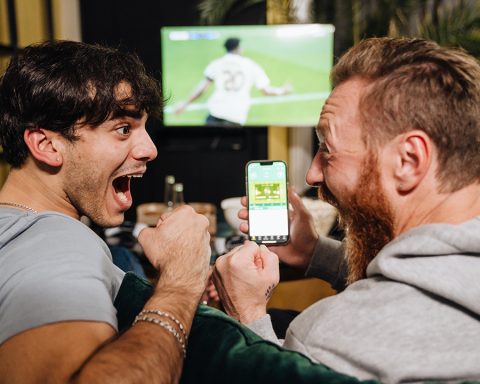 Två män tittar på fotbollsmatch och visar känslor